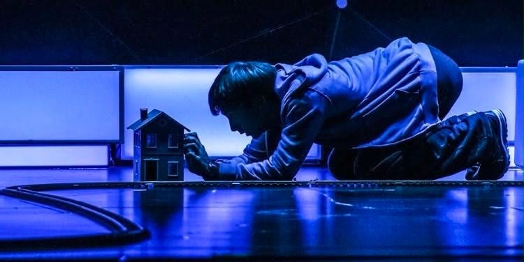 Iñaki Aldao se arrodilla ante una casa en miniatura y una vía de tren, reflejando la complejidad del mundo de Christopher Boone en la aclamada obra de teatro 'El curioso incidente del perro a medianoche' (Gentileza de Prensa)