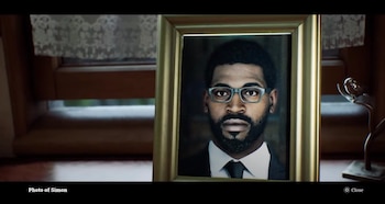 Un retrato enmarcado en dorado de un hombre con gafas, barba, traje y corbata sobre un mueble de madera junto a una ventana