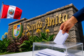 Una mano introduce un sobre en una urna transparente frente a un muro de piedra con el nombre Santa Anita y la bandera peruana.