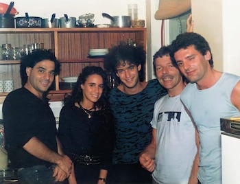 Cinco personas posan sonriendo dentro de una cocina frente a una estantería de madera con tazas, platos y ollas