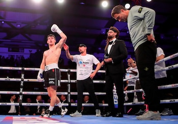 William Crolla, boxeador sin camiseta con pantalones negros y guantes blancos, levanta un brazo en el ring. Un hombre de gorra le observa