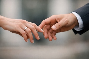 Dos manos adultas se acercan pero no se tocan. La mano izquierda lleva un anillo plateado en el dedo anular. El fondo es difuminado.
