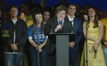 Javier Milei en un podio con micrófono. A su izquierda, Tarcísio de Freitas y una mujer con camiseta azul; a su derecha, un hombre con traje y una mujer de amarillo