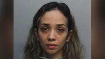 Primer plano de una joven con cabello largo ondulado, tatuajes faciales, un piercing sobre el labio superior y ojeras, mirando fijamente a la cámara