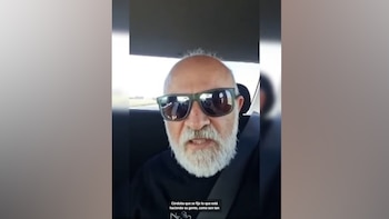 Hombre calvo con barba blanca y gafas de sol oscuras en primer plano, sentado en un coche con cinturón de seguridad, grabándose a sí mismo