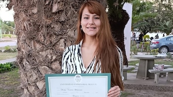 Una mujer sonriente de cabello castaño rojizo, vestida con blusa rayada, sostiene un diploma verde de la Universidad Empresarial Siglo 21 frente a un árbol
