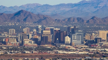 Vista aérea del centro de Phoenix con numerosos rascacielos y edificios de apartamentos bajo un cielo azul claro, con montañas de fondo