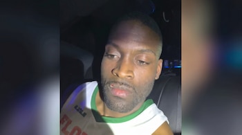 Un hombre con una herida en el labio superior viste una camiseta deportiva y permanece sentado dentro de un vehículo en penumbra.