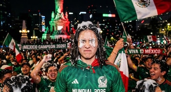 Persona con camiseta de fútbol de México y espuma en ojos y cabello, entre una multitud con banderas mexicanas y confeti en una celebración nocturna