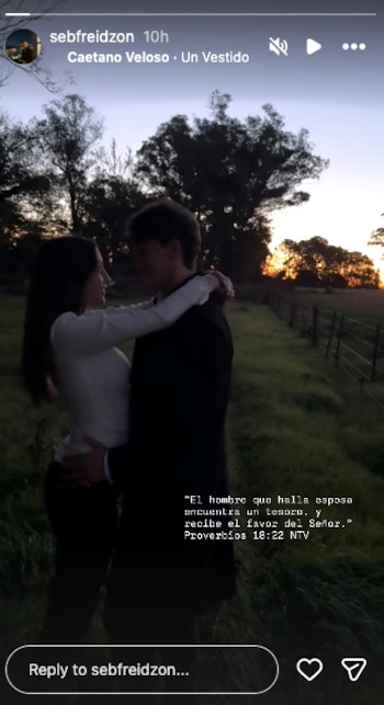 Una pareja se abraza al aire libre durante el atardecer, con la mujer de blanco y el hombre de oscuro, en un campo con árboles al fondo