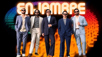 Cinco hombres, todos con gafas de sol, posan de pie. Detrás de ellos, el nombre ENJAMBRE en letras grandes y luminosas, con letras más pequeñas repetidas.