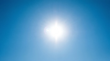 El sol brillante y deslumbrante ocupa el centro de un cielo azul claro, completamente despejado y sin nubes, con un ligero destello de lente.