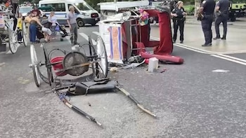Carruaje de caballos destruido y volcado en una calle de asfalto gris. Se observan piezas del vehículo desparramadas, civiles y dos oficiales de policía