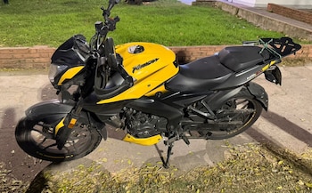 Motocicleta deportiva amarilla y negra con un portaequipajes trasero, estacionada en una acera de cemento junto a césped verde en la oscuridad de la noche