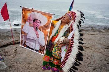 Un chamán realiza un ritual mientras sostiene un cartel del candidato presidencial Roberto Sánchez en la playa La Herradura de Lima, Perú, el lunes 1 de junio de 2026, antes de la segunda vuelta de las elecciones presidenciales. (AP Foto/Martín Mejía)