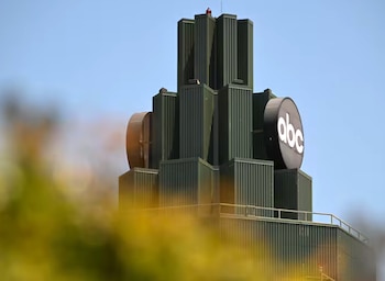 Parte superior de un edificio verde con un diseño de bloques escalonados, un logotipo circular negro con las letras blancas "abc", y cielo azul