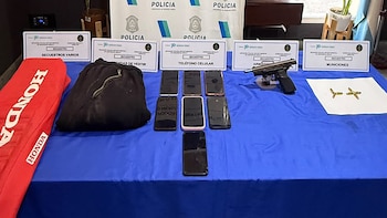 Una pistola negra, un cargador, siete balas y un cable blanco sobre una superficie de baldosas de color claro