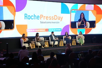 Cuatro personas sentadas en un escenario durante una conferencia frente a una pantalla gigante