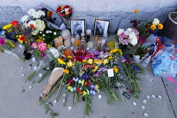 Diversos ramos de flores, velas encendidas y dos fotografías enmarcadas descansan en el suelo de concreto junto a una pared