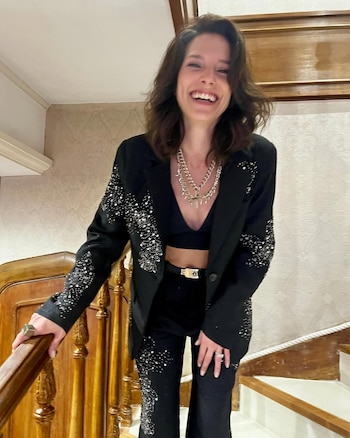 Manuela Pal sonríe en una escalera. Viste blazer y pantalones negros con apliques plateados, un top corto y un collar de cadenas plateadas