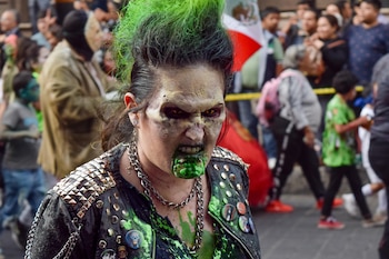 Primer plano de una persona con cresta verde, maquillaje protésico y líquido verde en la boca, frente a una multitud