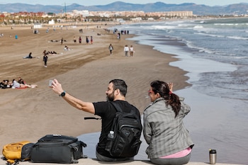 Dos personas se toman una foto ante la playa de Las Arenas de Valencia, a 13 de abril de 2026. (EFE/Manuel Bruque)
