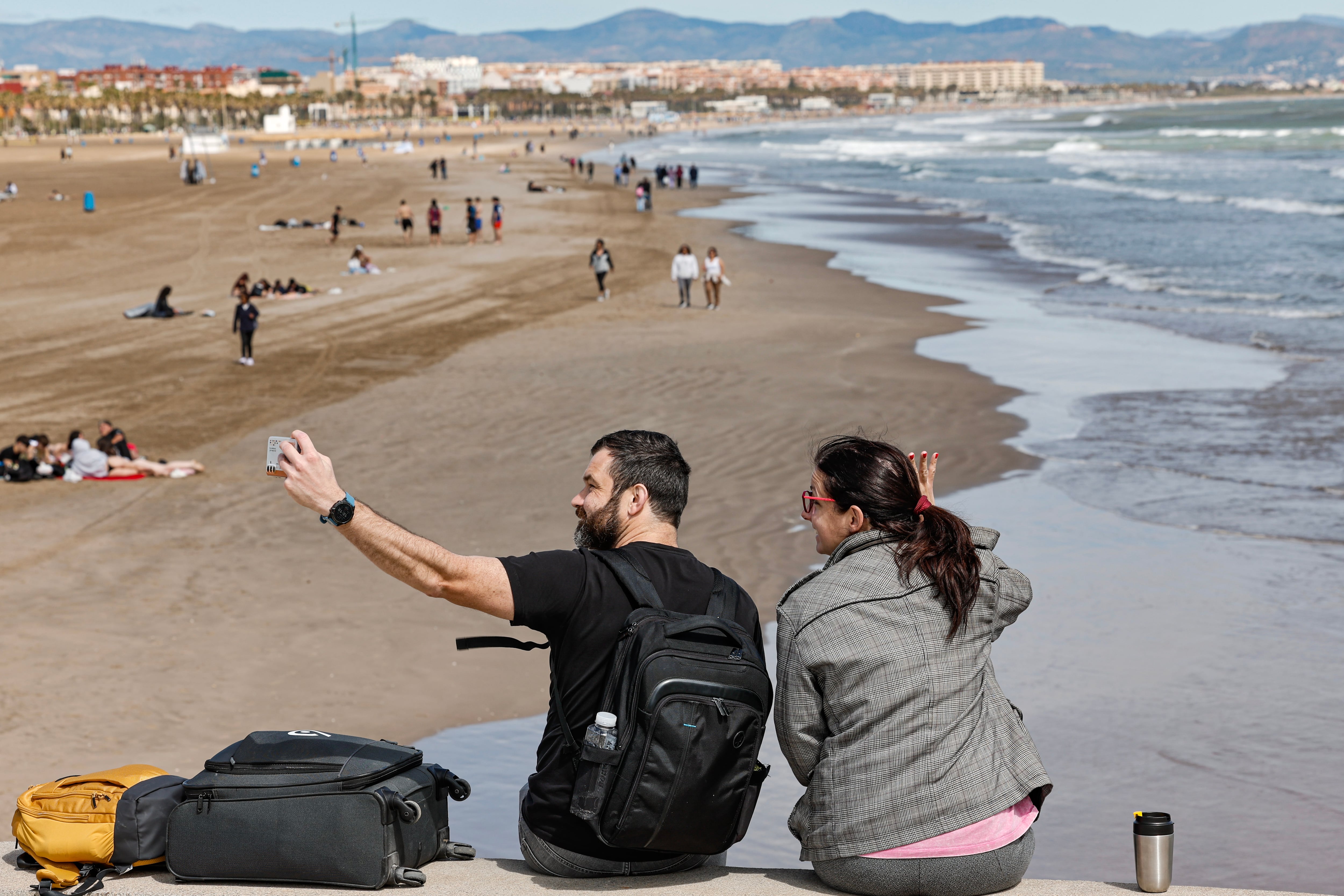 Dos personas se toman una foto ante la playa de Las Arenas de Valencia, a 13 de abril de 2026. (EFE/Manuel Bruque)