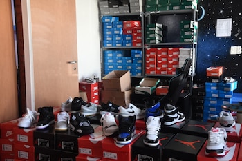 Una habitación con docenas de pares de zapatillas deportivas de diversas marcas y sus cajas apiladas en estanterías y el suelo
