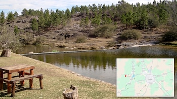 Río con pequeña represa, mesa de madera en la orilla, colina con pinos y mapa en la esquina inferior con un marcador en Flor Serrana.