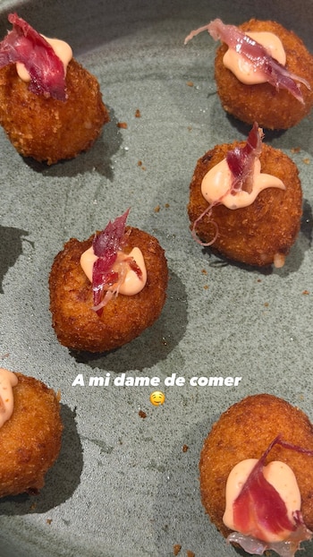 Seis croquetas fritas con salsa rosada y tiras de embutido sobre un plato gris. Texto blanco: "A mi dame de comer" y un emoji