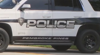 Vista lateral de un vehículo policial blanco con las palabras "POLICE" y "PEMBROKE PINES" en los costados y un emblema. Tiene ruedas negras