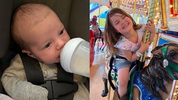 Un bebé con mono gris bebe de un biberón en un asiento con arnés; al lado, una niña con camiseta y shorts sonríe en un caballo de carrusel