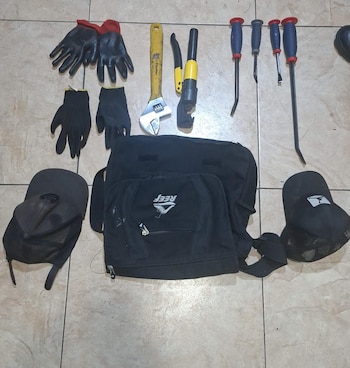 Varias herramientas, dos pares de guantes, dos gorras y un bolso negro con el logo 'Reef' sobre un suelo de baldosas claras