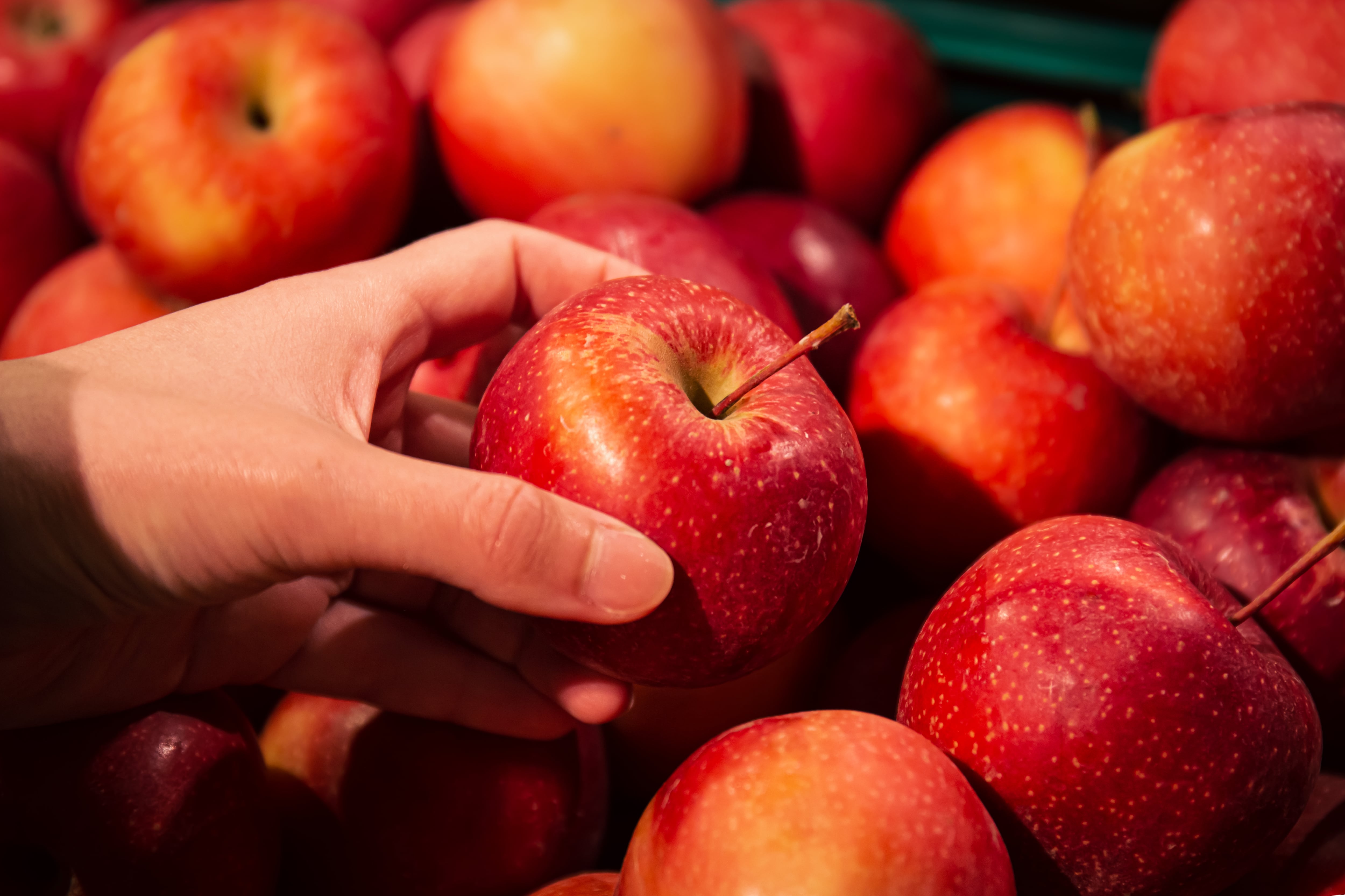 Una mujer sostiene una manzana roja en una frutería (Magnific)