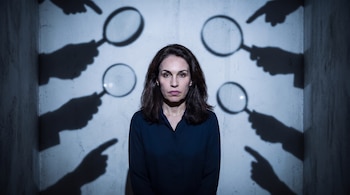 Viviane Morales observa al frente mientras sombras de varias manos con lupas y dedos índices apuntan hacia ella en una pared.