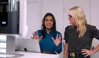 Dos mujeres de pie frente a una computadora portátil y un dispositivo de análisis facial blanco en una habitación con paredes claras
