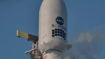 Cofia de un cohete blanco con los logotipos de la NASA y del telescopio Roman que emite vapor cerca de una torre metálica