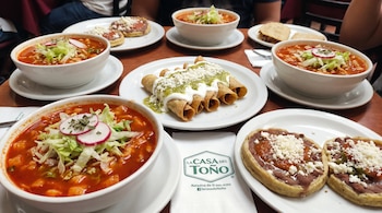 Cuatro tazones de pozole rojo. Un plato con flautas, crema y salsa verde. Dos platos con sopes, frijoles y queso. Servilleta con el logo La Casa del Toño.