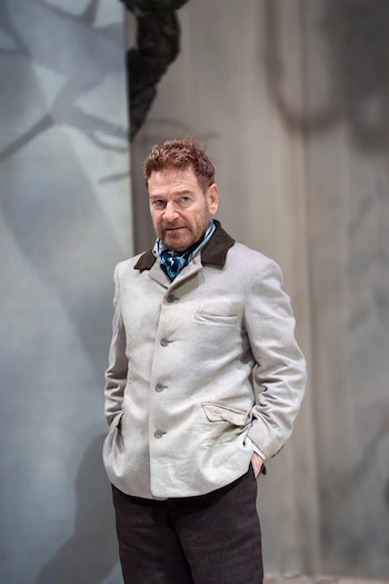 Retrato de un hombre con barba y cabello castaño rojizo, viste una chaqueta clara con cuello oscuro, camisa azul y pañuelo. Fondo escénico