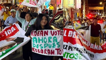Multitud de personas marchando de noche, con Roberto Sánchez Palomino al frente, sosteniendo pancartas y megáfonos, bajo la luz de un vehículo policial
