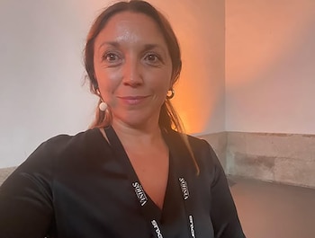 Analía Videla, mujer de cabello castaño oscuro, viste una blusa negra con lanyards y mira a cámara con una leve sonrisa, sobre un fondo de pared clara con iluminación cálida