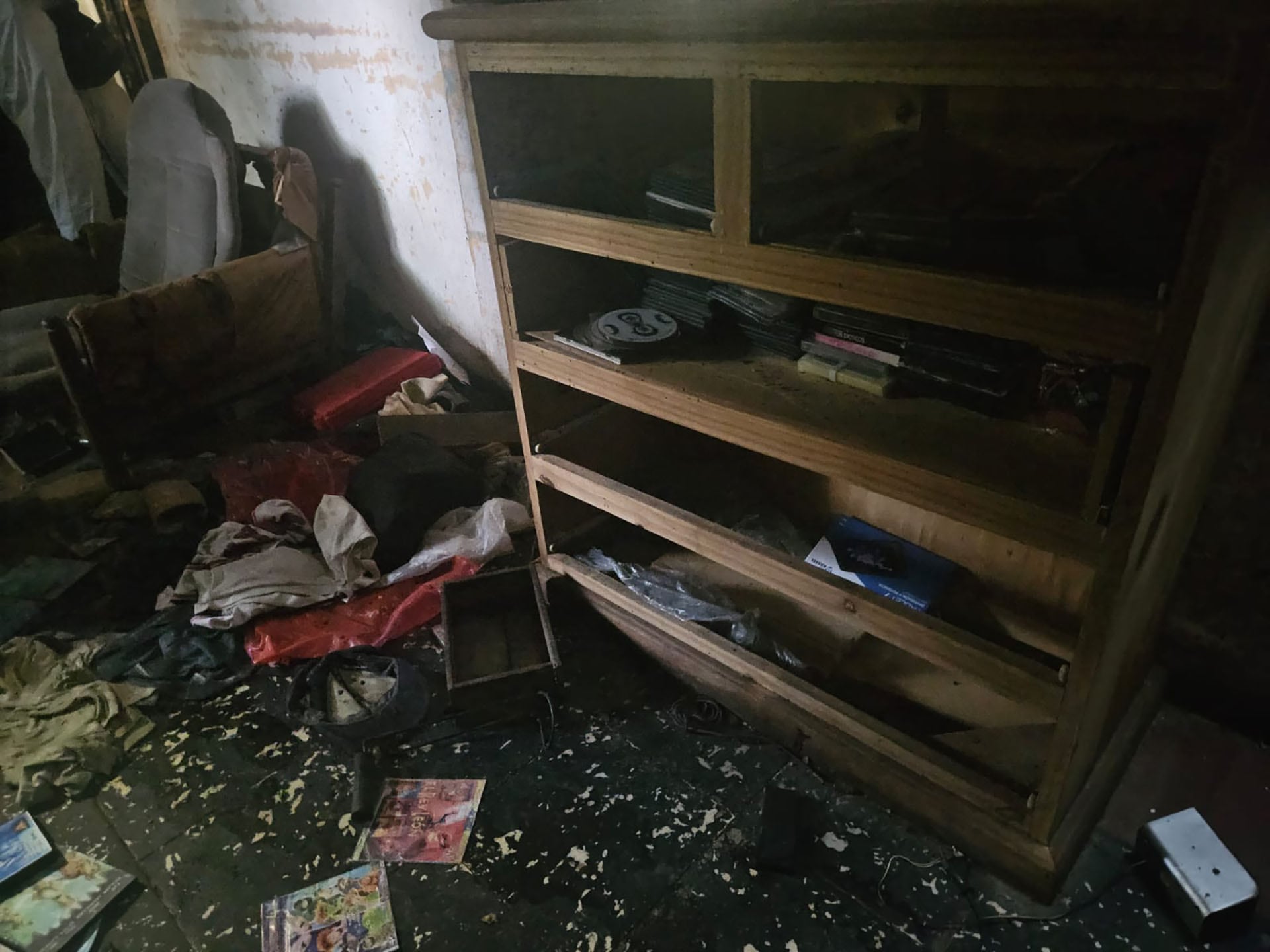 Una vista de la habitación desordenada en lo que se ha identificado como la escena del crimen del rapero Mike Dee, mostrando un estante de madera y objetos esparcidos por el suelo.