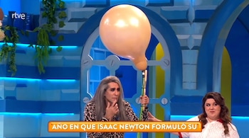 Hombre con cabello gris largo y traje de leopardo, mujer con cabello castaño, sentados en un decorado azul. Globo beige desinflado. Texto "AÑO EN QUE ISAAC NEWTON FORMULÓ SU".