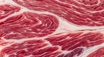 Vista de cerca de una pieza de carne roja cruda con pronunciado marmoleado blanco y textura detallada de fibras musculares.