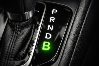 Primer plano de la palanca de cambios de un coche automático con las letras P, R, N, D y B. La letra B está iluminada en verde brillante.