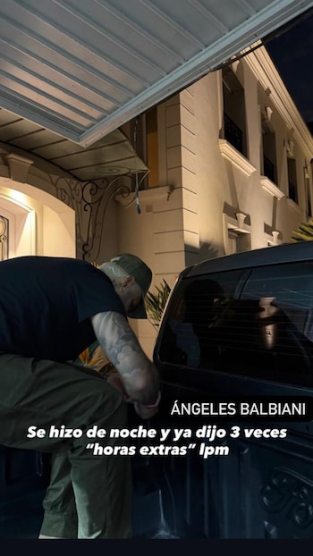 Persona de espaldas con gorra y tatuajes agachada en la parte trasera de un vehículo oscuro por la noche, frente a un edificio iluminado