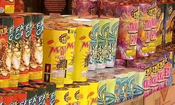 Diversas cajas y tubos de fuegos artificiales de colores amarillo, rojo, verde y morado apilados, con etiquetas de marcas y advertencias de precaución