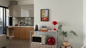 Vista interior da cozinha moderna com armários cinza e de madeira, perto de prateleiras metálicas com micro-ondas, chaleira, luz vermelha e plantas.