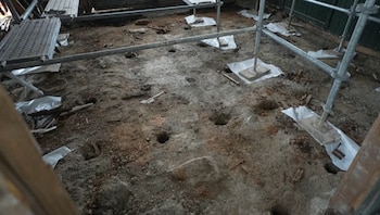 Suelo de tierra con varios agujeros y restos de escombros, junto a andamios metálicos, en un área interior en obras de cimentación