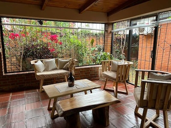 Sala de estar con muebles de madera, mesas, piso de baldosas rojas y grandes ventanales con vista a un jardín
